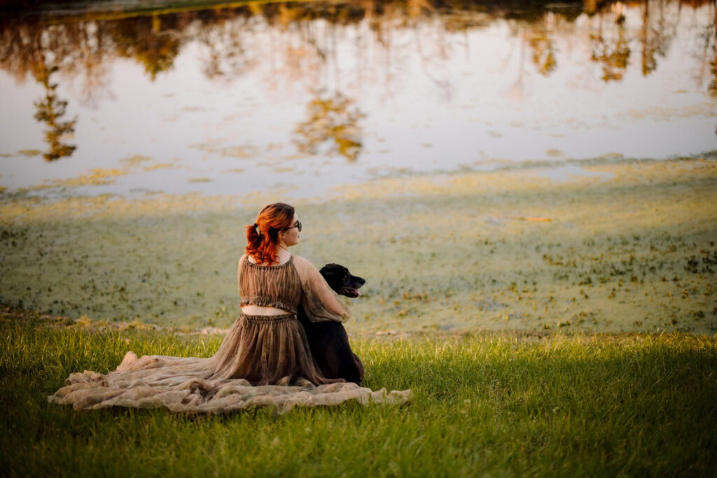 Beautiful woman and dog sitting by the lake at sunset.