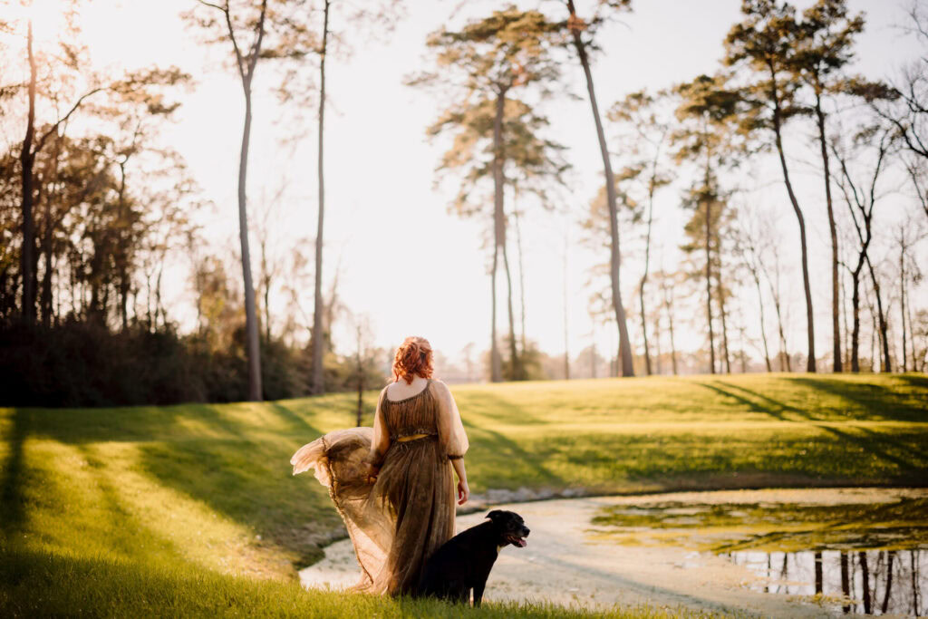 A woman with red hair walking along a lake trail with her dog during sunset.