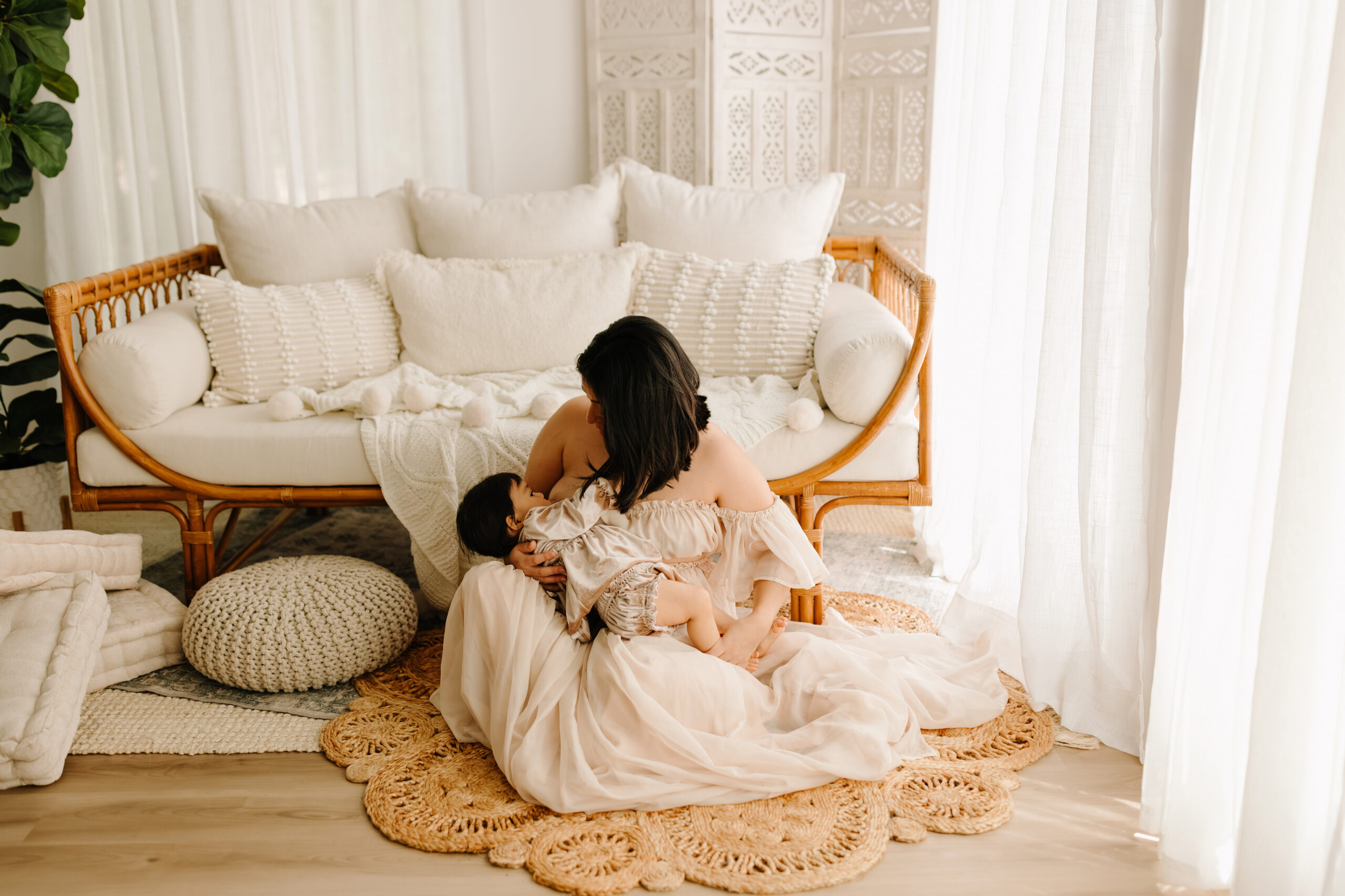Mother breastfeeding her baby on a soft rug in a bright, airy living room.