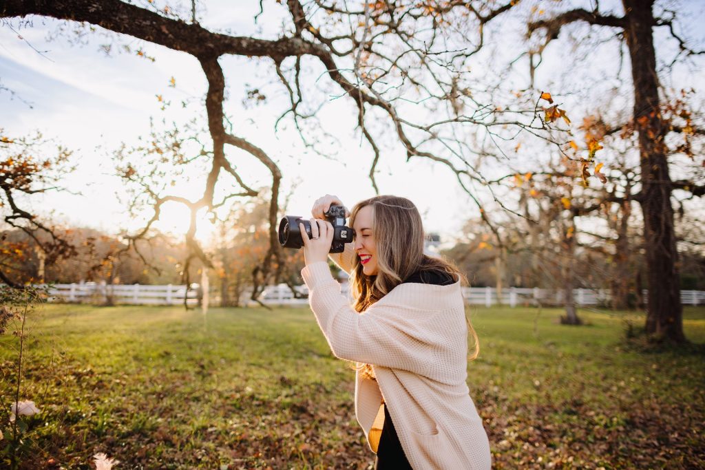 Young woman taking photos outdoors during sunset in a park.