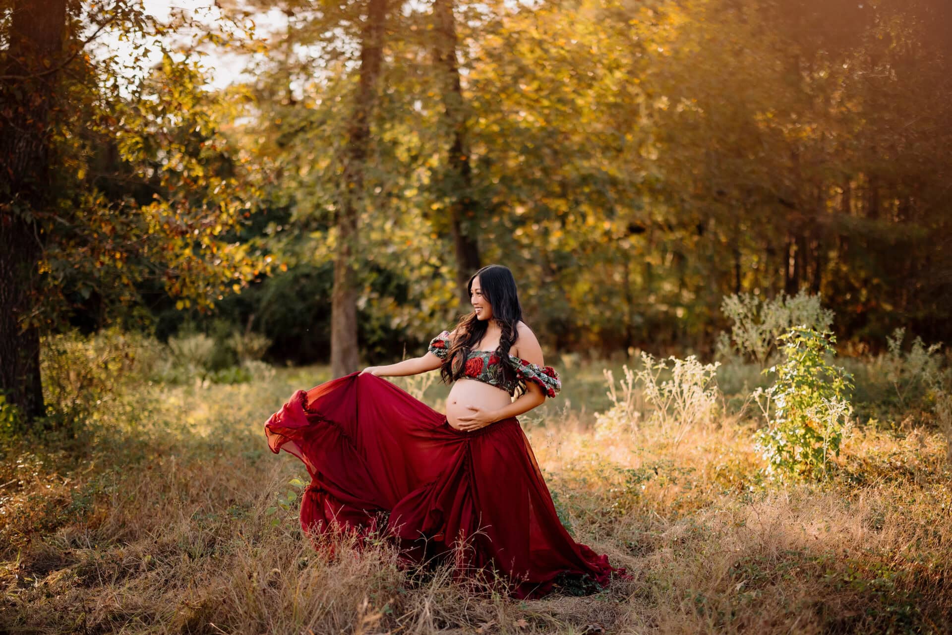 Pregnant woman in flowing red dress outdoors.