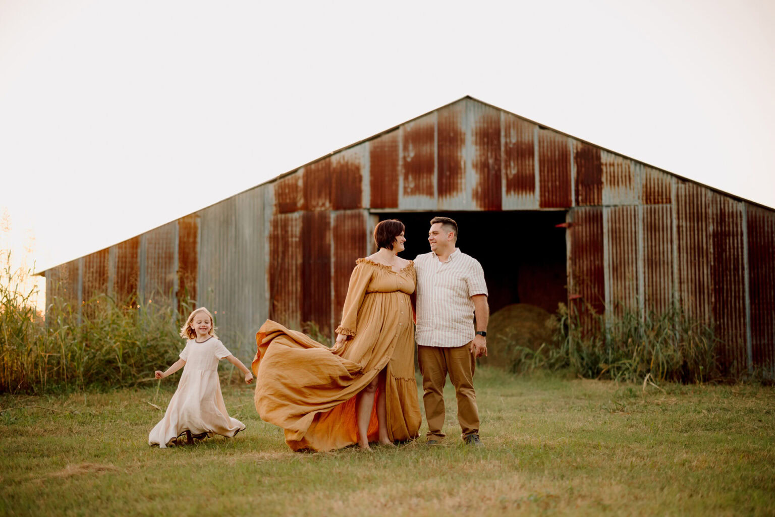 Family portrait outdoors in front of a rustic barn, capturing a joyful moment during a photoshoot.