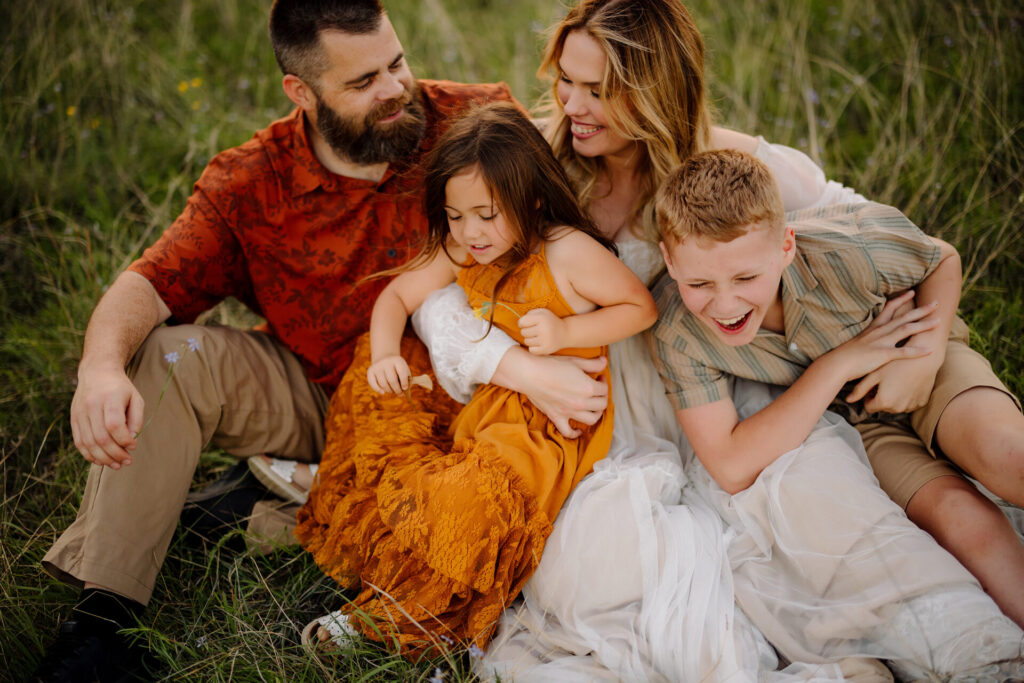 a family of four snuggles and laughs together in tall grass