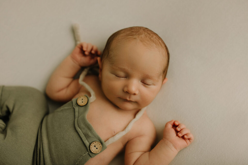 a newborn baby lays on a blanket in green overalls