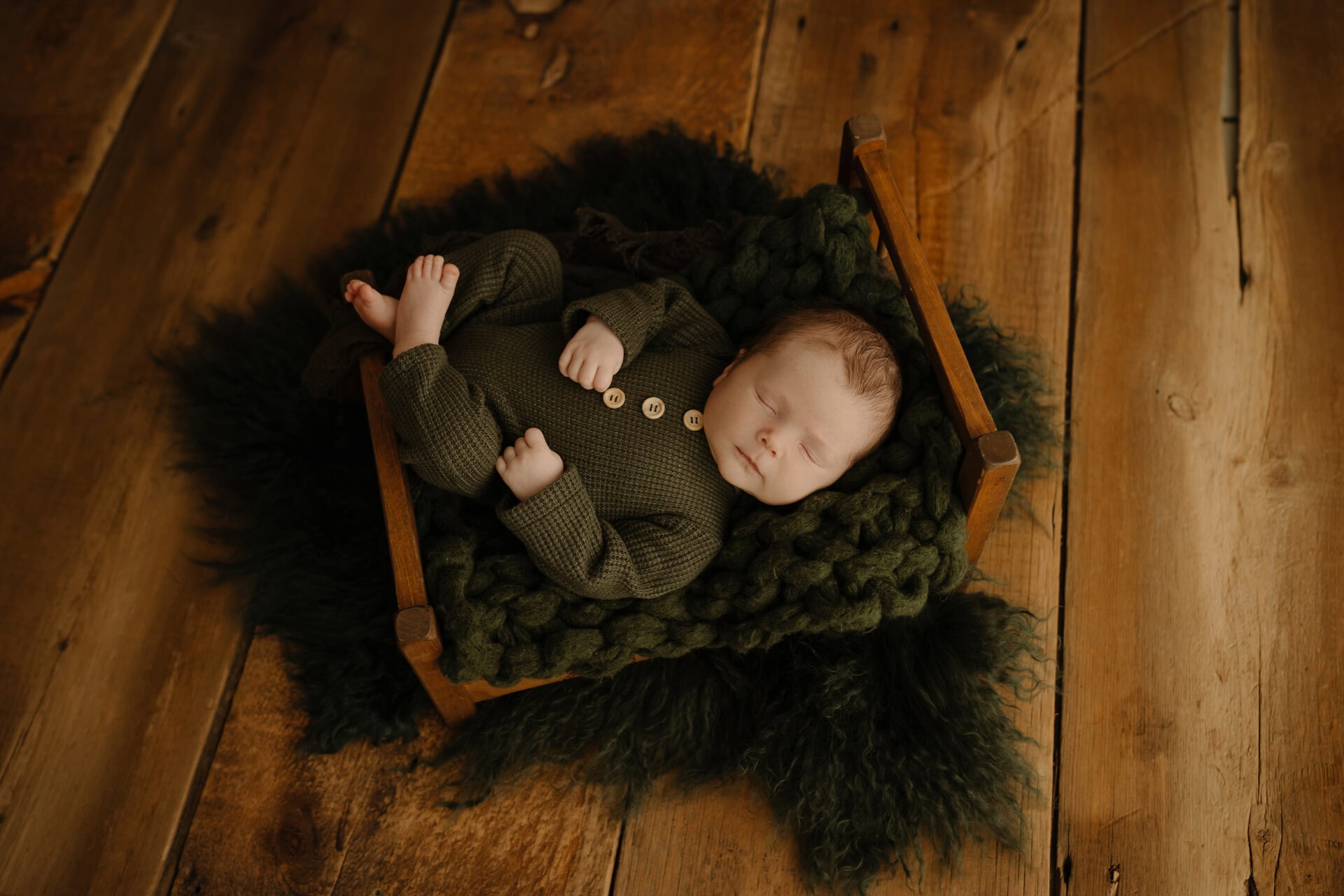Adorable newborn baby peacefully sleeping on a cozy black blanket on a wooden floor.