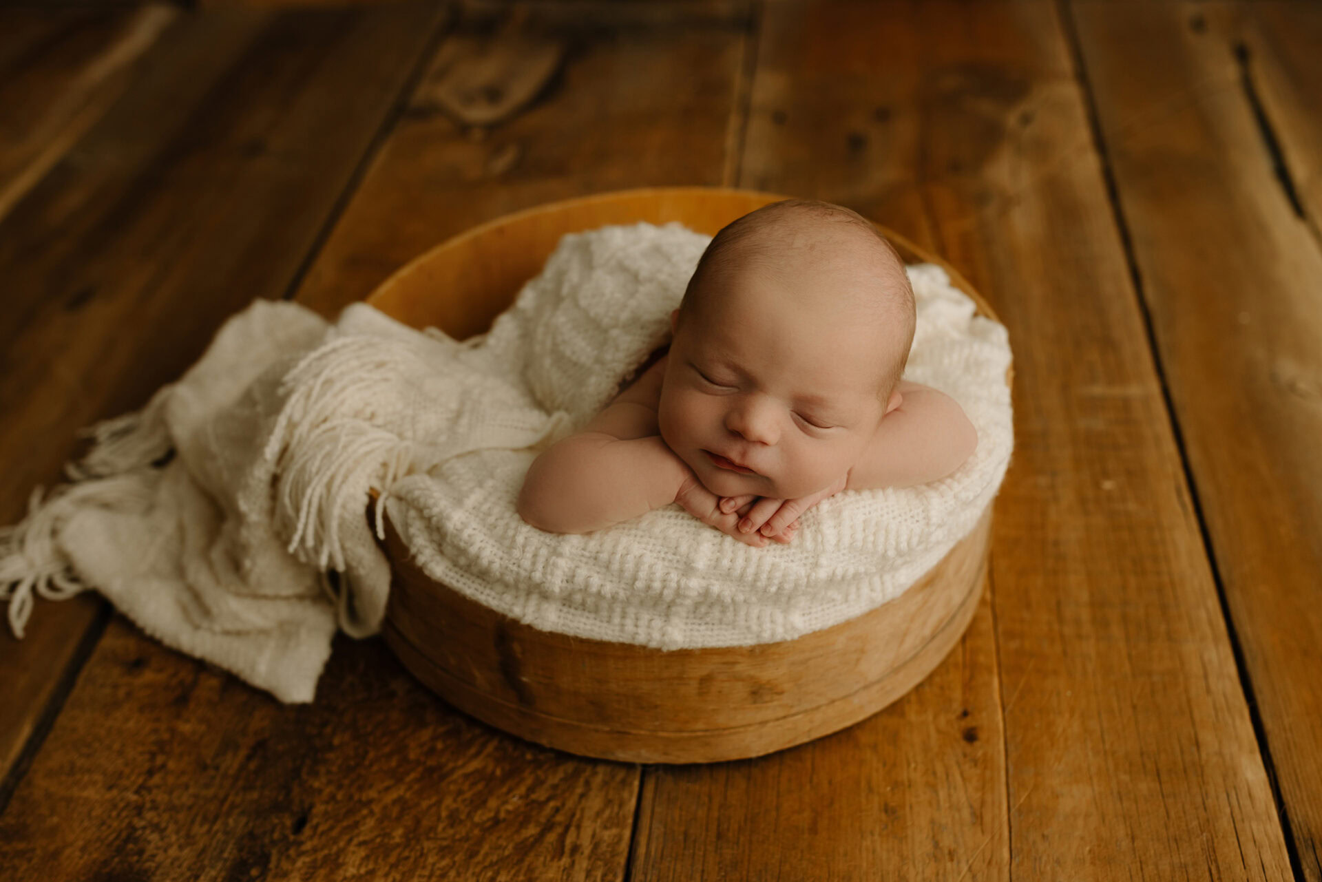 Baby sleeping peacefully in a cozy wooden bowl.