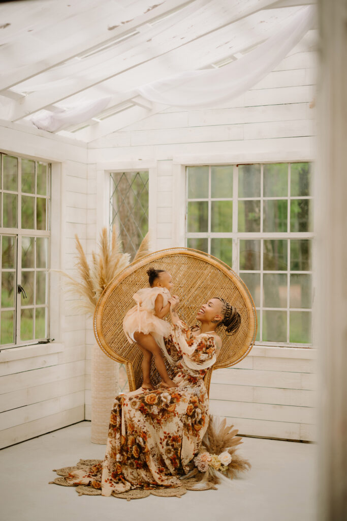Mother and daughter sharing joyful moment in sunlit white-washed room with large windows.