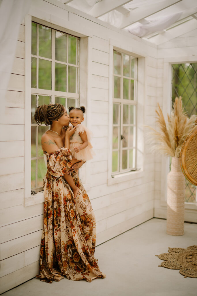 Mother and daughter smiling and playing together in a bright, cozy room with large windows.