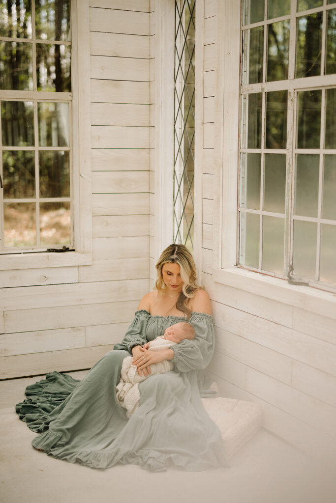 Mother and newborn in a bright, airy room with large windows and white wooden walls.