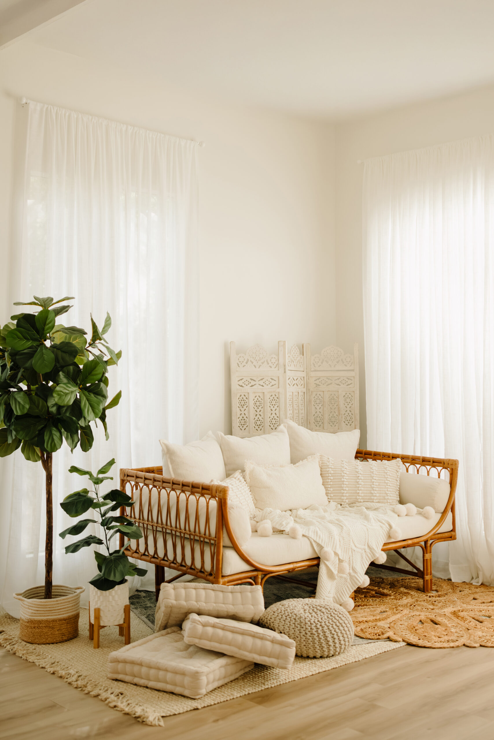 Bright and airy living room with white curtains, rattan sofa, and plush cushions. Natural light crea.