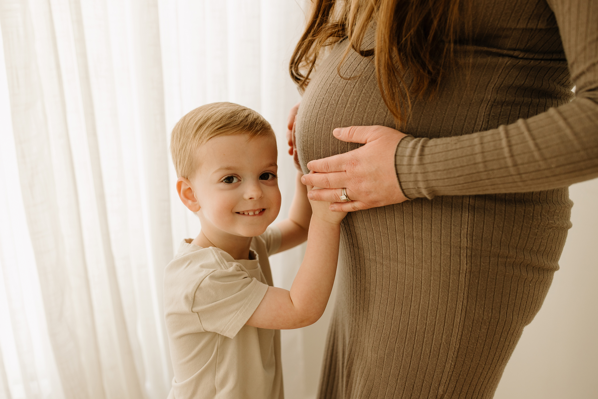 Pregnant woman with young son gently touching her baby bump, celebrating the last trimester before w.