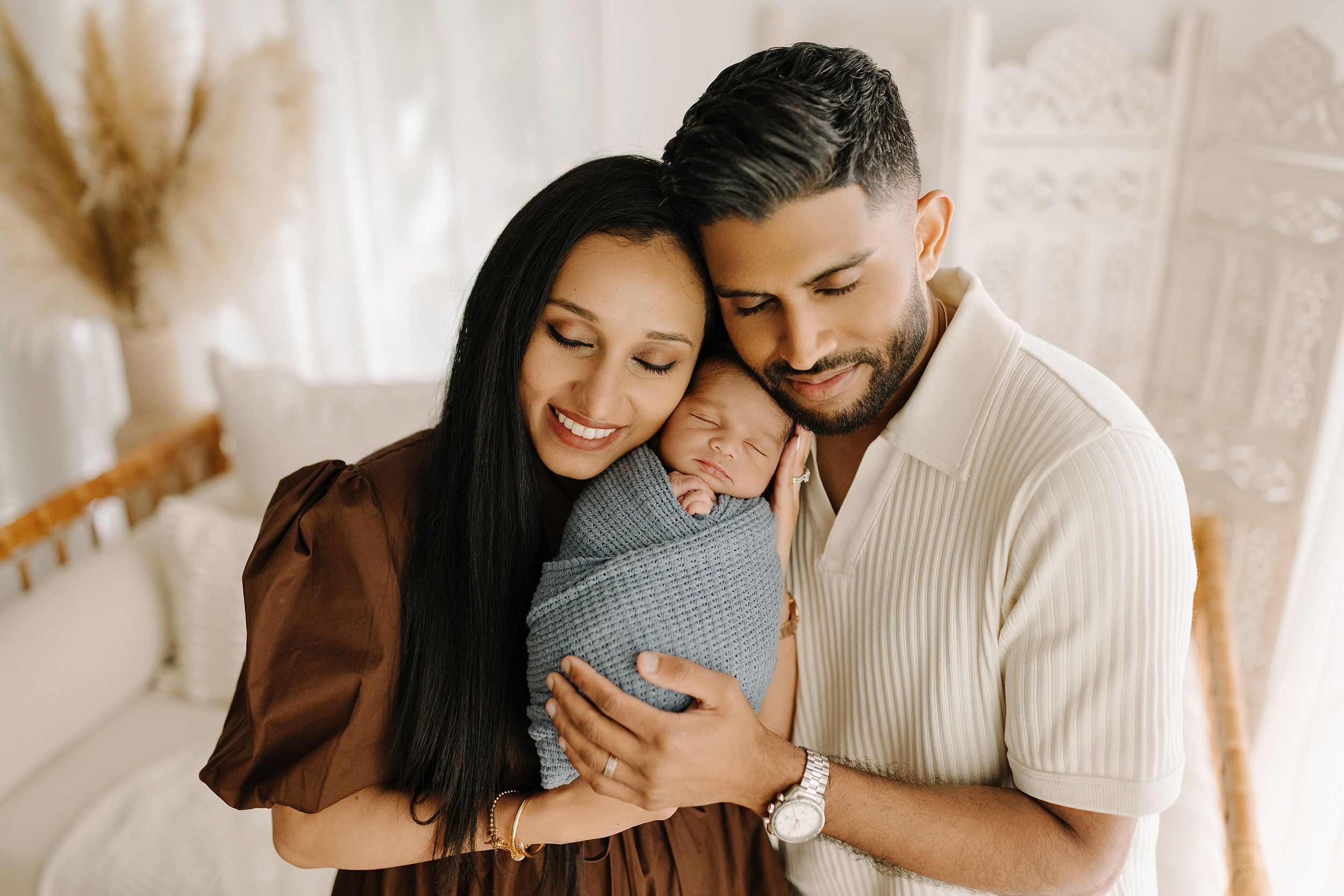 A baby wrapped in a blanket being held by happy parents.