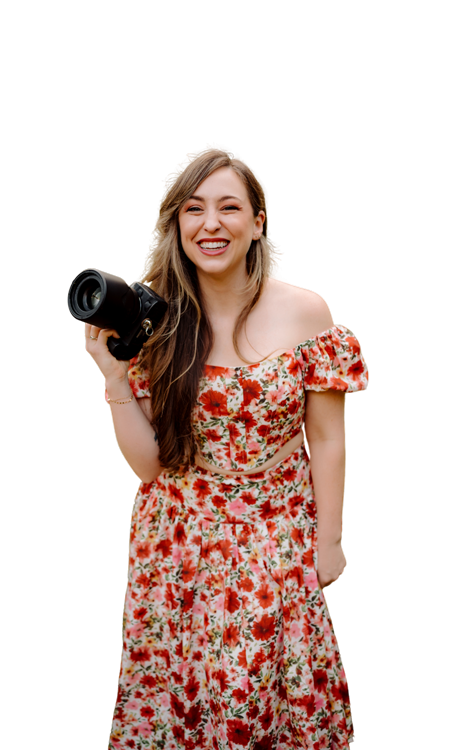 Portrait of a smiling young woman holding a camera, wearing a floral dress.