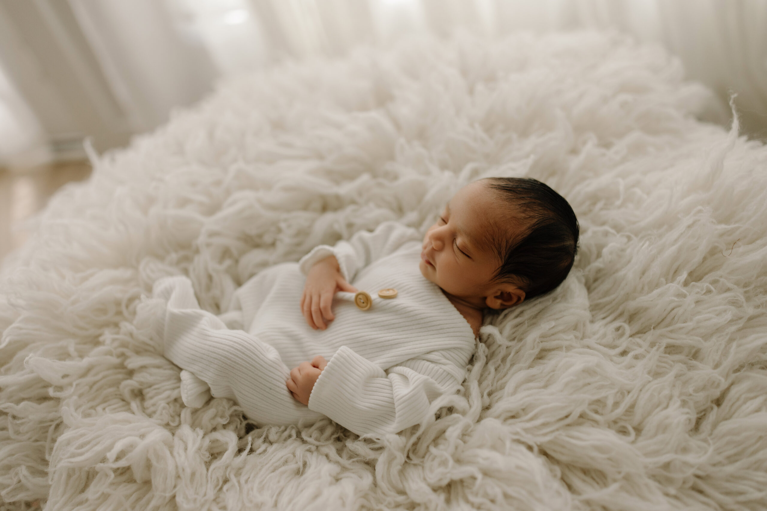 Baby sleeping peacefully on a fluffy white blanket in a cozy indoor setting.