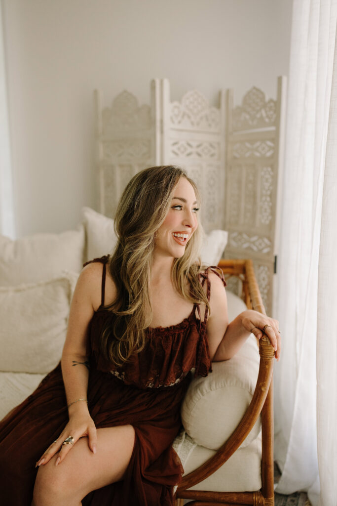 Portrait of a smiling woman sitting on a cream sofa in a bright room.
