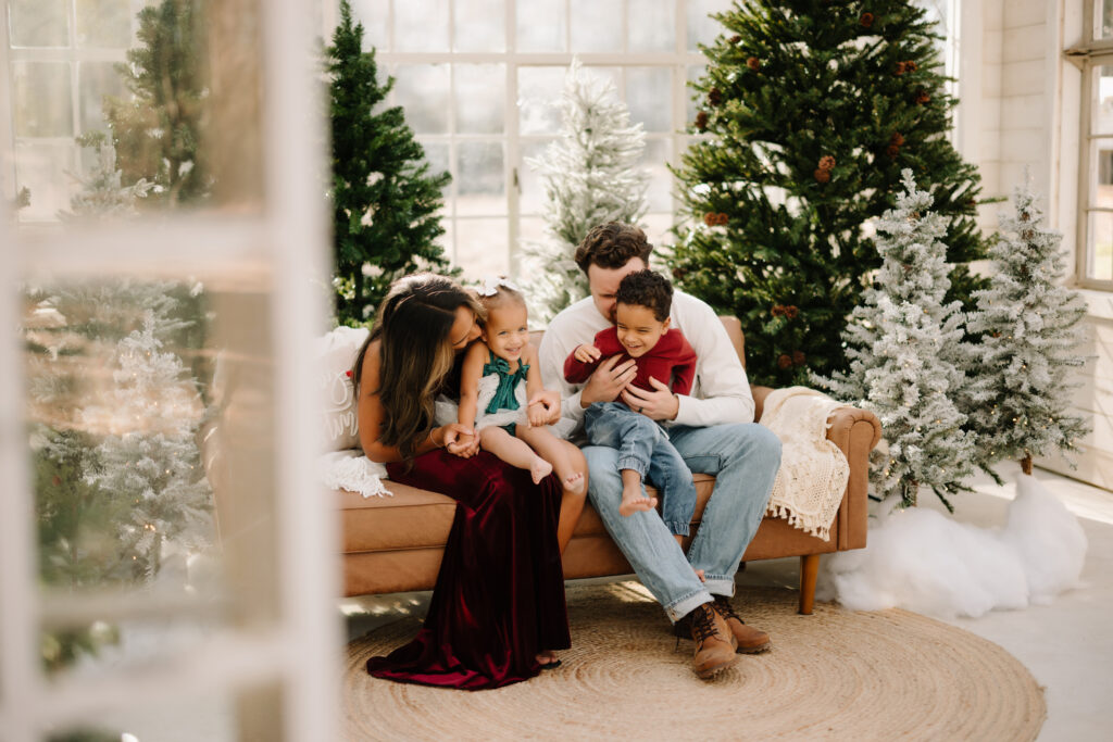 Family sitting on sofa with Christmas trees in background in The Woodlands TX.