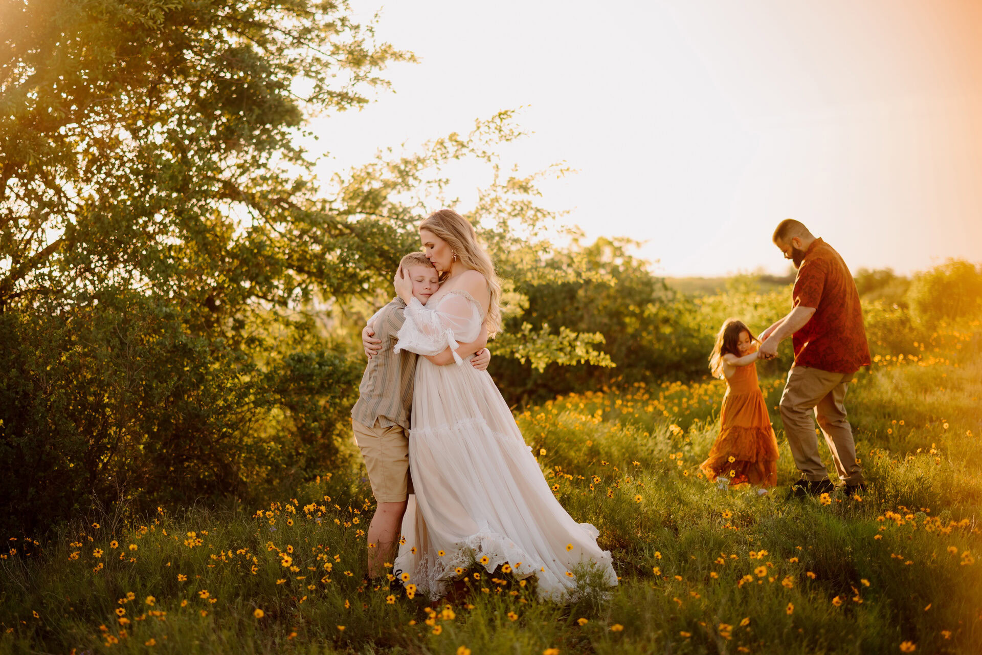 Family embracing outdoors during sunset, with children playing nearby.